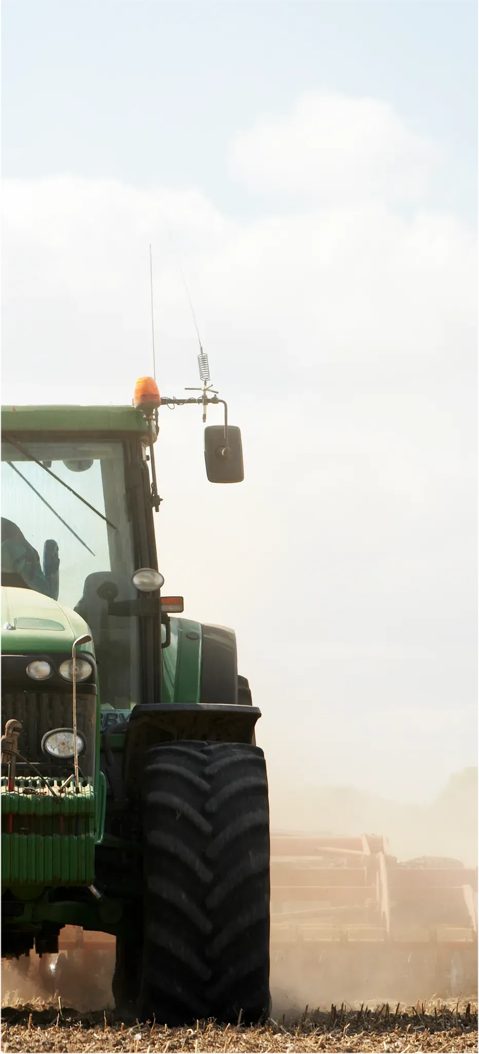 Grüner Traktor mit Anhänger auf einem staubigen Feldweg